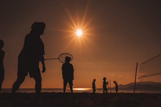 silhouettes of elderly Asian people playing badminton on the beach by sea in morning at sunrise