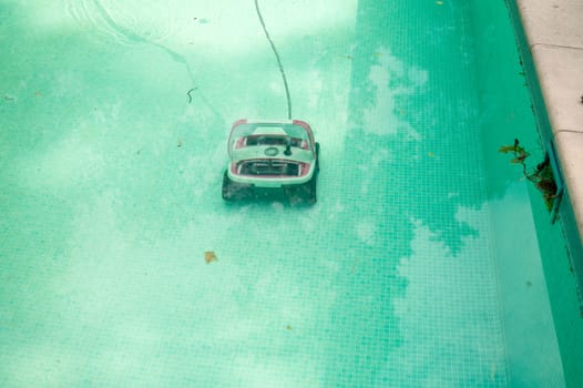 Water robot vacuum cleaner cleans, removes debris on the bottom, walls of the pool, top view through translucent water. Pool cleaning process. Preparing for the summer season. Smart home technologies