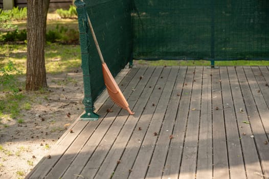 orange rake on a wooden platform, against the background of a park. pine cones are lying on a wooden platform.