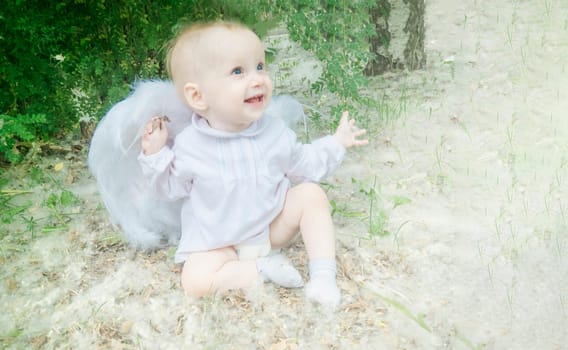 Fairy tale concept. Little toddler girl wearing beautiful dress with angel wings in the forest or park, spring day, white blooming trees, poplar fluff clouds