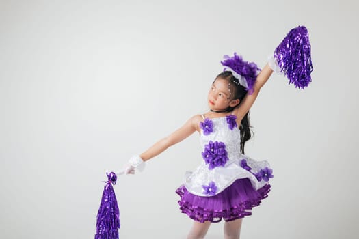 Young girl dressed in cheerleading gear, purple pom-poms in hand. Studio photo with white background, full of festive energy. cheerleader kid