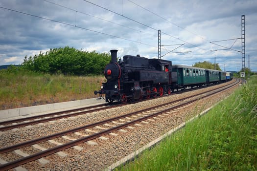 Old Czech historical steam train with wagons driving on the tracks for a trip. Concept for railways and history.