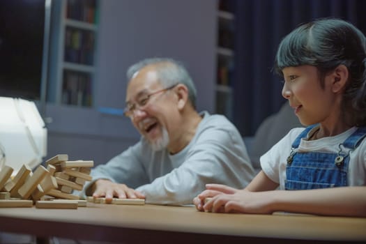 Happy grandparents Asian family enjoy playing toy block with little daughter and mother together at home night time, Smiling parent having fun play build constructor tower of wooden blocks, education