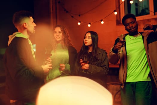 Group of four friends enjoy a lively evening outdoors sharing drinks and engaging in conversation. The vibrant atmosphere is enhanced by string lights illuminating their smiles.