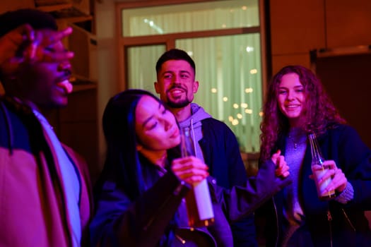 A group of four friends is celebrating indoors, surrounded by vibrant lights. They are laughing, dancing, and enjoying drinks together, creating a joyful atmosphere.