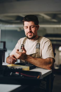 A focused craftsman checks his tools in a well-lit workspace. He holds a drill while surrounded by various equipment and materials, showing dedication to his craft.