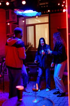 A group of three friends celebrates under vibrant lights, laughing and dancing together at an outdoor gathering. The atmosphere is lively, showcasing their joy and excitement.