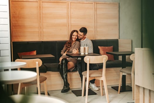 A young couple sits closely together in a contemporary cafe, sharing smiles and warmth on a relaxed afternoon, creating a cozy and intimate atmosphere.