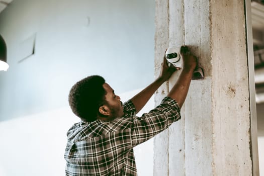 A skilled worker is focused on installing a security camera on a concrete pillar in a contemporary workspace. It is midday, and the atmosphere is professional.