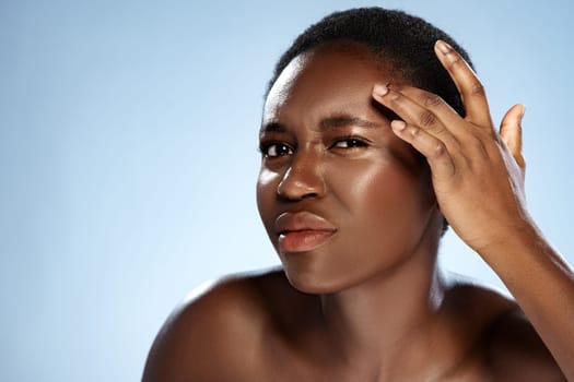 A woman displays her natural beauty with a thoughtful expression as she gently touches her forehead. Soft blue tones highlight her glowing skin, promoting self-care and confidence.