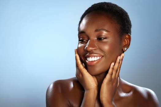 A woman with short hair beams with joy, gently touching her face while showcasing her radiant smile. The background is a soft blue, enhancing the mood of happiness and confidence.