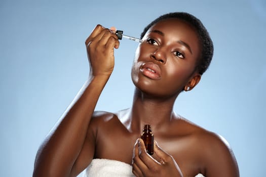 A woman uses a dropper to apply facial serum to her skin, showcasing a beauty routine that emphasizes self-care and skin health. She appears calm and focused in a tranquil atmosphere.