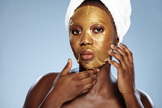 A woman is seen applying a gold sheet mask on her face, enhancing her skincare routine. She is in a well-lit indoor space, wearing a towel around her head.