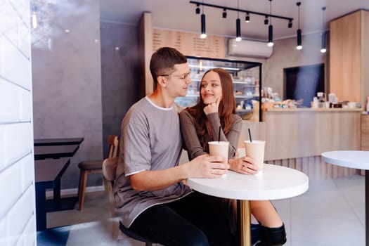 A couple sits closely at a small table in a stylish cafe, enjoying their drinks and engaging in a friendly conversation during a relaxed afternoon.