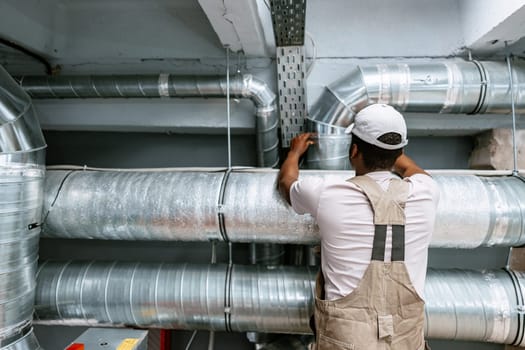 A technician is working diligently to install metal ducting in a commercial building, ensuring proper air circulation and system efficiency. This project takes place indoors.