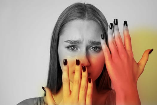 A young woman performs a creative expression of emotion with her hands contrasting against her face. The black and white setting enhances the vivid hues surrounding her hands.