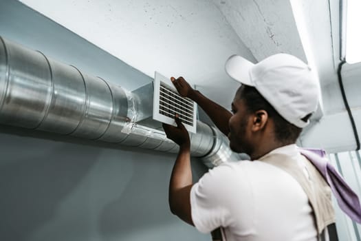 A worker is focused on installing a ventilation grate within a duct in a commercial space. The task is crucial for maintaining air quality and comfort for building occupants.
