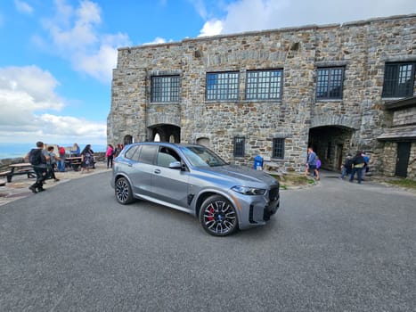 Wilmington, NY USA - 05.23.2024: Modern BMW X5 SUV at Scenic Overlook with Stone Building and Distant Landscape Views at Whiteface Mountain.