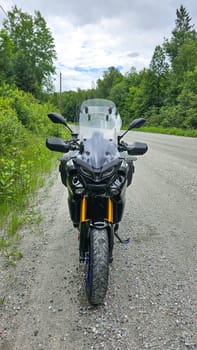 Sargent s Purchase, NH USA - 08.22.2024: Adventure Motorcycle Yamaha Tracer 9 GT on a Gravel Road Surrounded by Lush Greenery, Cloudy Sky Above.