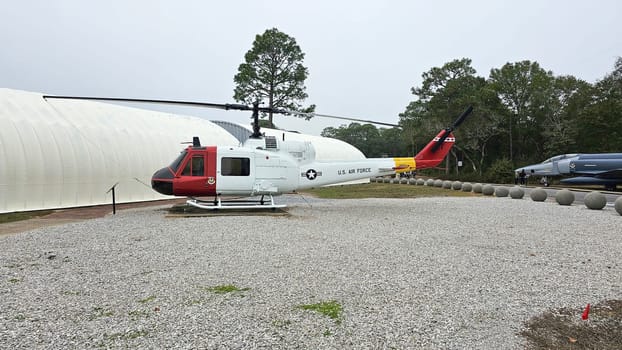 Eglin AFB, FL USA - 12.27.2024: Vintage Helicopter Displayed Outdoors with Unique Red and Yellow Tail Design, and Gray Gravel.