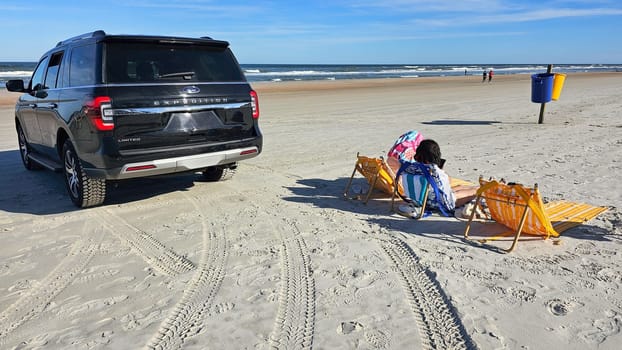 Daytona Beach, FL USA - 01.01.2025: SUV on Beach with People Relaxing Coastal Getaway Scene with Vehicle and Beachgoers.
