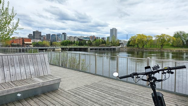 Ottawa, ON Canada - 05.14.2025: Cityscape View from Riverside Boardwalk with Bicycle Foreground and Cloudy Skies Above.