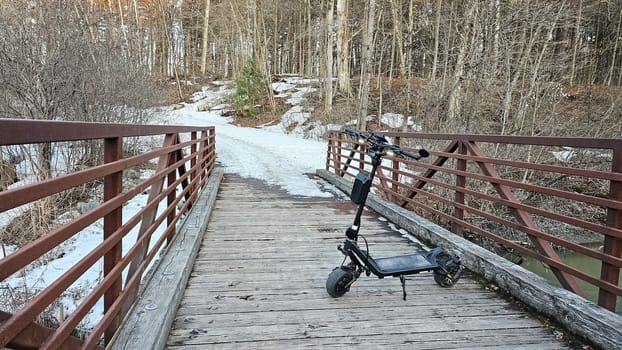 An electric scooter is parked on a wooden bridge amidst a wintry landscape, symbolizing eco-friendly travel and adventure in nature. Perfect for promoting sustainable tourism.