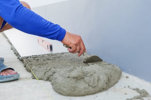 A worker hand uses a trowel to smooth gray mortar, preparing a level surface for floor tiles. Precision and craftsmanship in tiling work are on display.