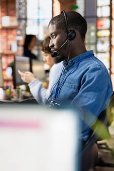 Helpful call center agent at office desk talking in headphones mic, handling customers support requests. Customer service worker using audio headset to assist clients with issues related to products