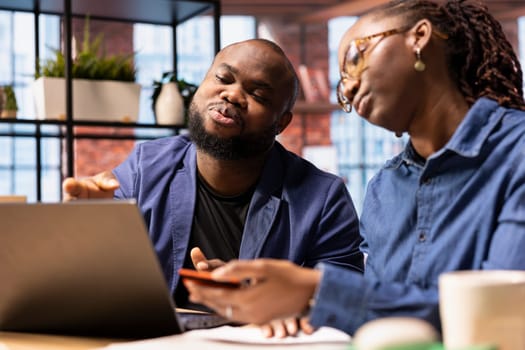 Young people using a card to check the balance before buying or paying something, e commerce from the home office. African american man and woman do web transactions remotely.