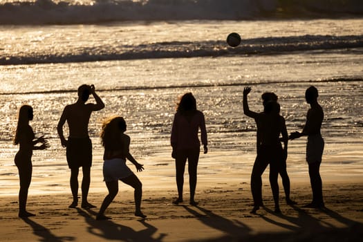 Silhouetted friends enjoy a beach volleyball game at sunset, creating lasting memories
