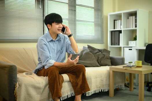 Young man sitting on sofa at home, having a phone conversation in a cozy living room.