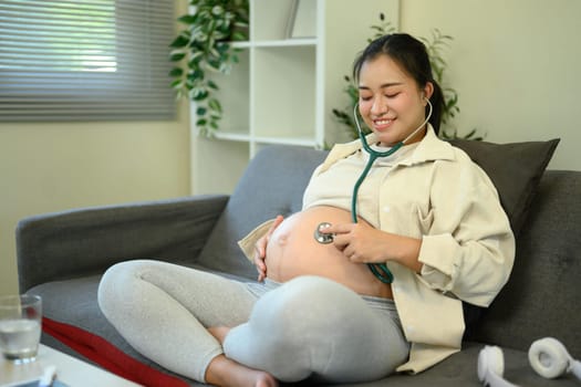 Pregnant woman using a stethoscope to listen to her baby heartbeat at home.