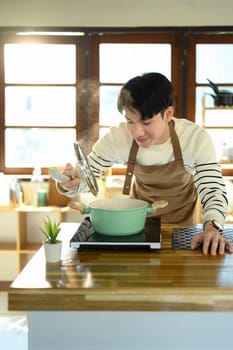 Happy Asian man preparing a meal on a modern stovetop.