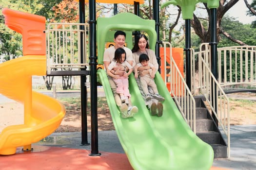 Happy family sliding down together at a colorful playground.