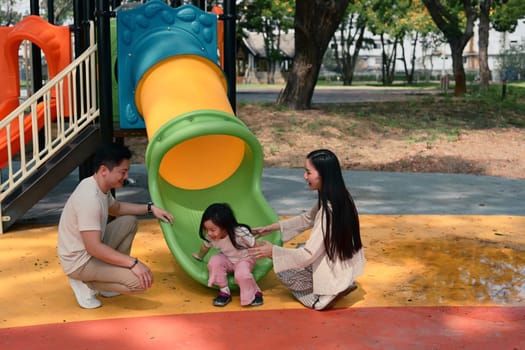 Smiling parents and two young children enjoy playtime at a colorful playground.