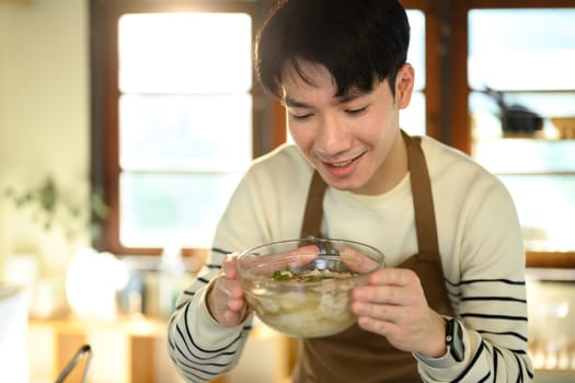 Happy asian man presenting a freshly prepared bowl of noodle soup.