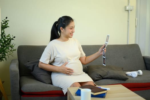 Happy pregnant woman holding her belly and looking at ultrasound photos.