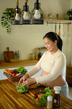 Expecting mother preparing a salad with fresh vegetables in home kitchen.