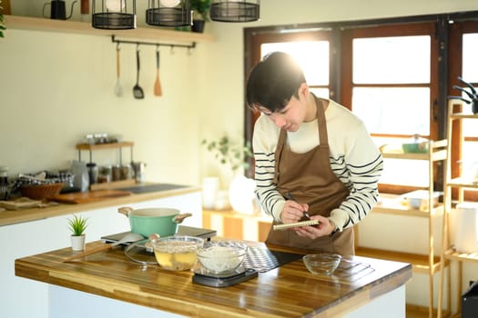 Asian man checking or jotting down a recipe during cooking.