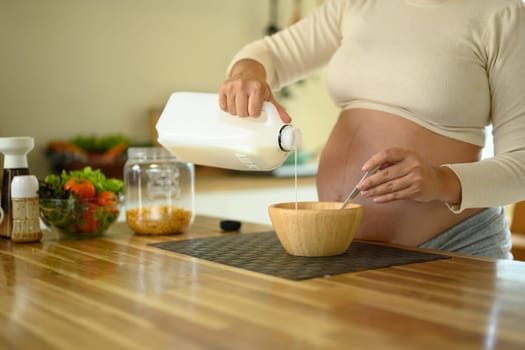 Hands of a pregnant woman making a morning meal in a bright kitchen.