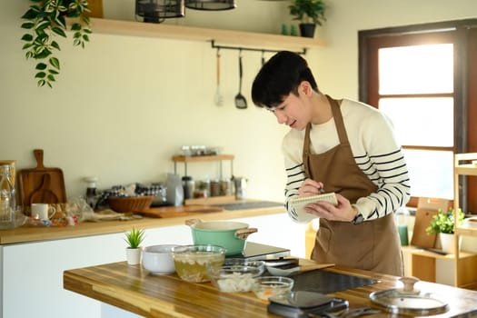 Asian man checking or jotting down a recipe during cooking.