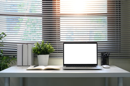 Minimalist workspace with a blank laptop screen, notebook, and plants by the window.