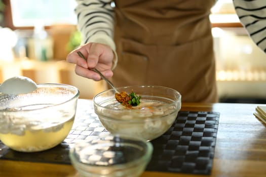 Close up of hand adding herbs and fried garlic to a bowl of hot soup.