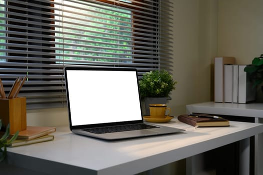 Modern home office desk with a blank laptop screen, notebook, and plants by the window.