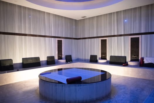 Modern Hammam Room with Stone Table. Modern hammam steam room with a central round stone massage table and stylish decor.