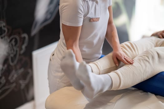 A therapist guiding a patient through leg exercises with the help of a blue foam roller in a therapy clinic.