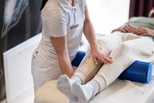 A therapist guiding a patient through leg exercises with the help of a blue foam roller in a therapy clinic.