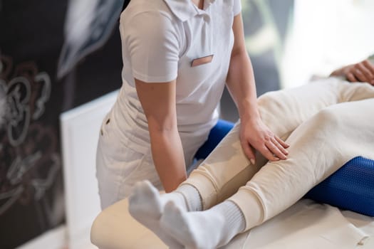 A therapist guiding a patient through leg exercises with the help of a blue foam roller in a therapy clinic.
