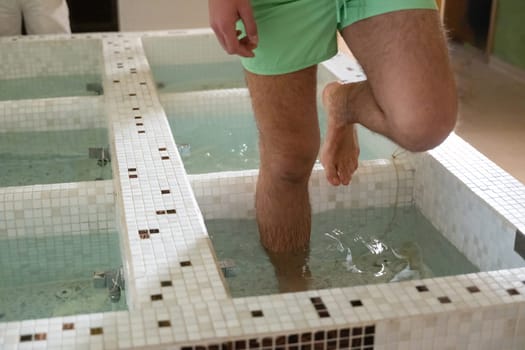 Close up of a mans legs as he steps into tiled spa therapy pools for a hydrotherapy session.